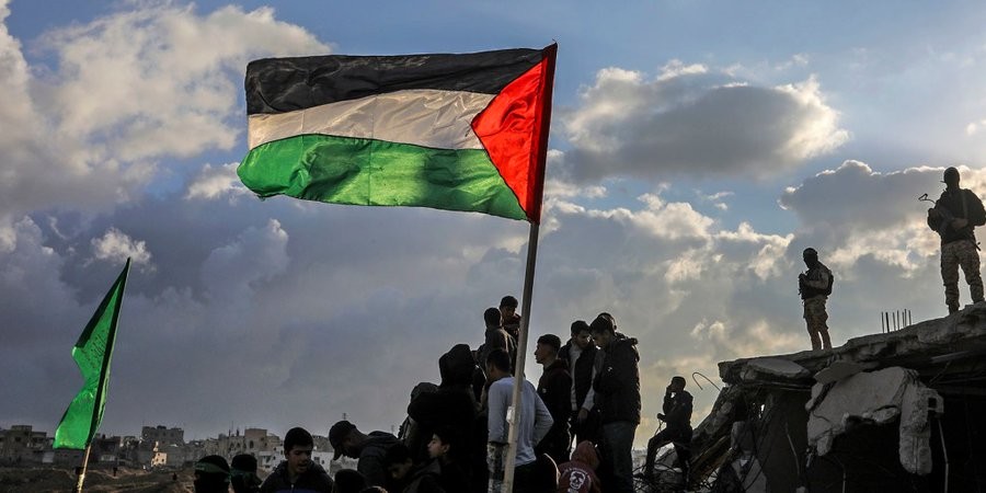 Người dân Palestine tụ tập dưới quốc kỳ trong khung cảnh đổ nát sau một đợt không kích ở Dải Gaza. Ảnh: NBC News