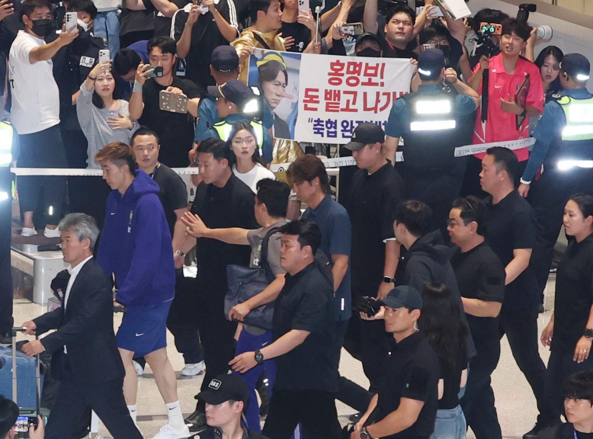Ông Hong Myung Bo đi ngang qua một tấm biển với dòng chữ “Hong Myung Bo, hãy trả lại tiền và biến đi!” tại Sân bay Quốc tế Incheon sáng 30/6. Ảnh: Korea Times