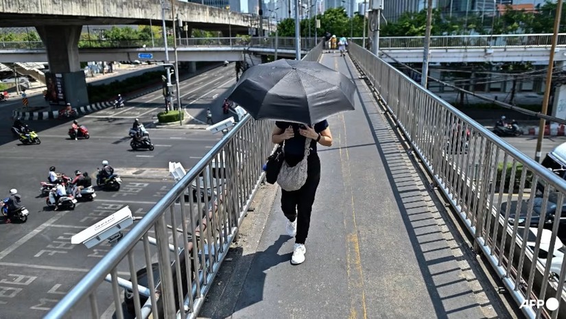 Một người phụ nữ che &ocirc; đi qua một c&acirc;y cầu ở Bangkok, Th&aacute;i Lan, ng&agrave;y 25/4. Ảnh: AFP
